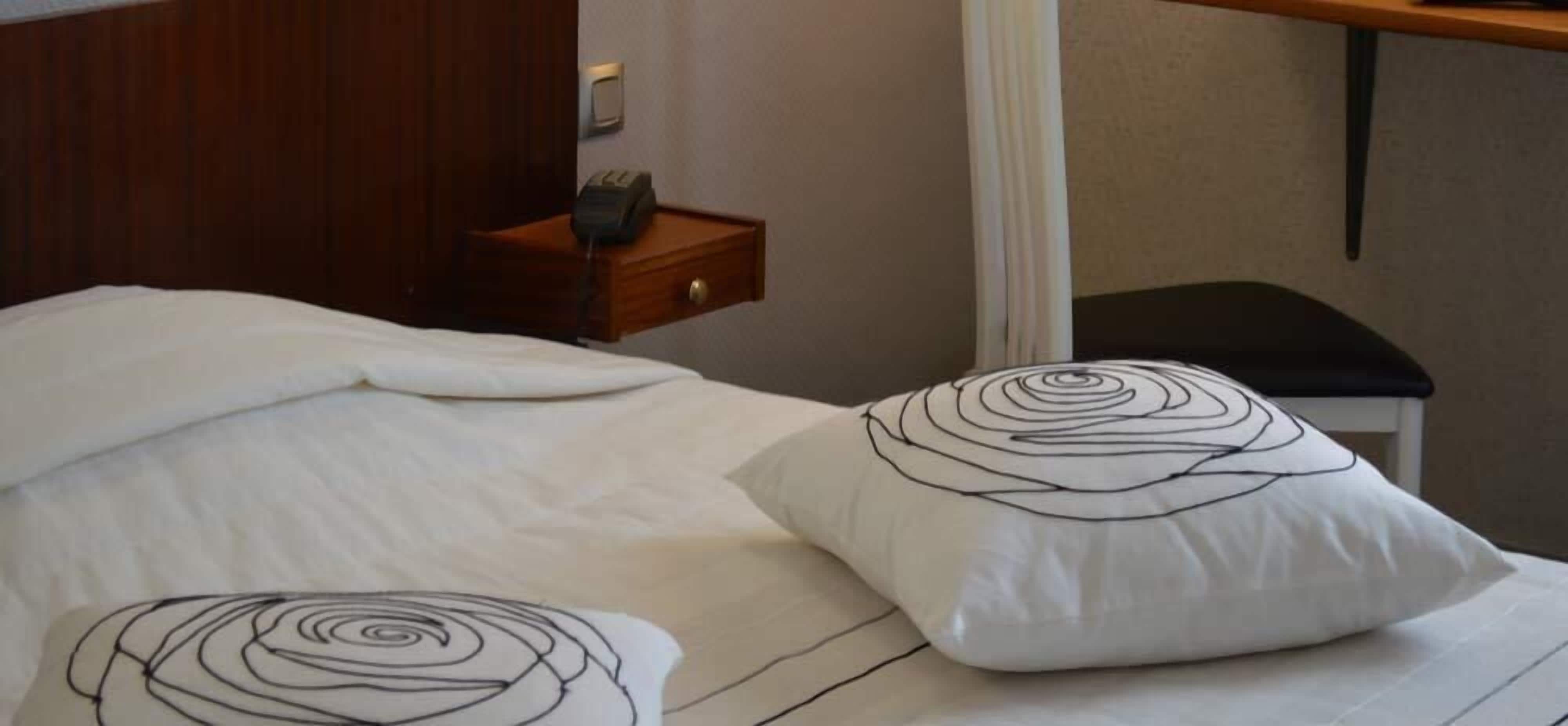 A neatly made bed with white bedding and two decorative pillows with a spiral design.