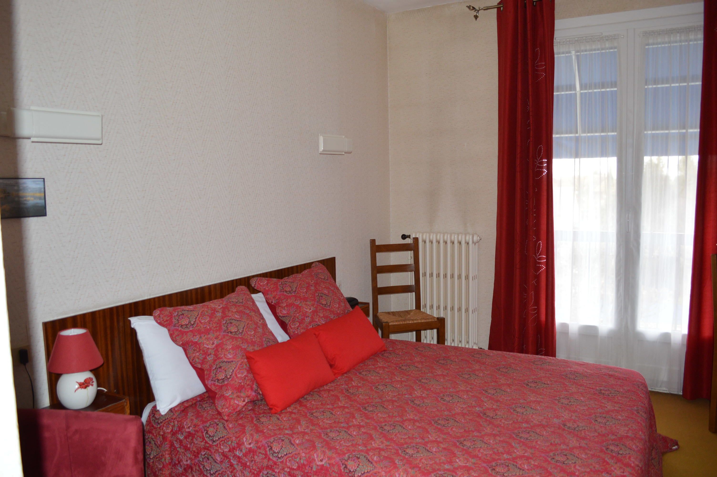 A bedroom with a bed, a nightstand, a chair, and a window with curtains.