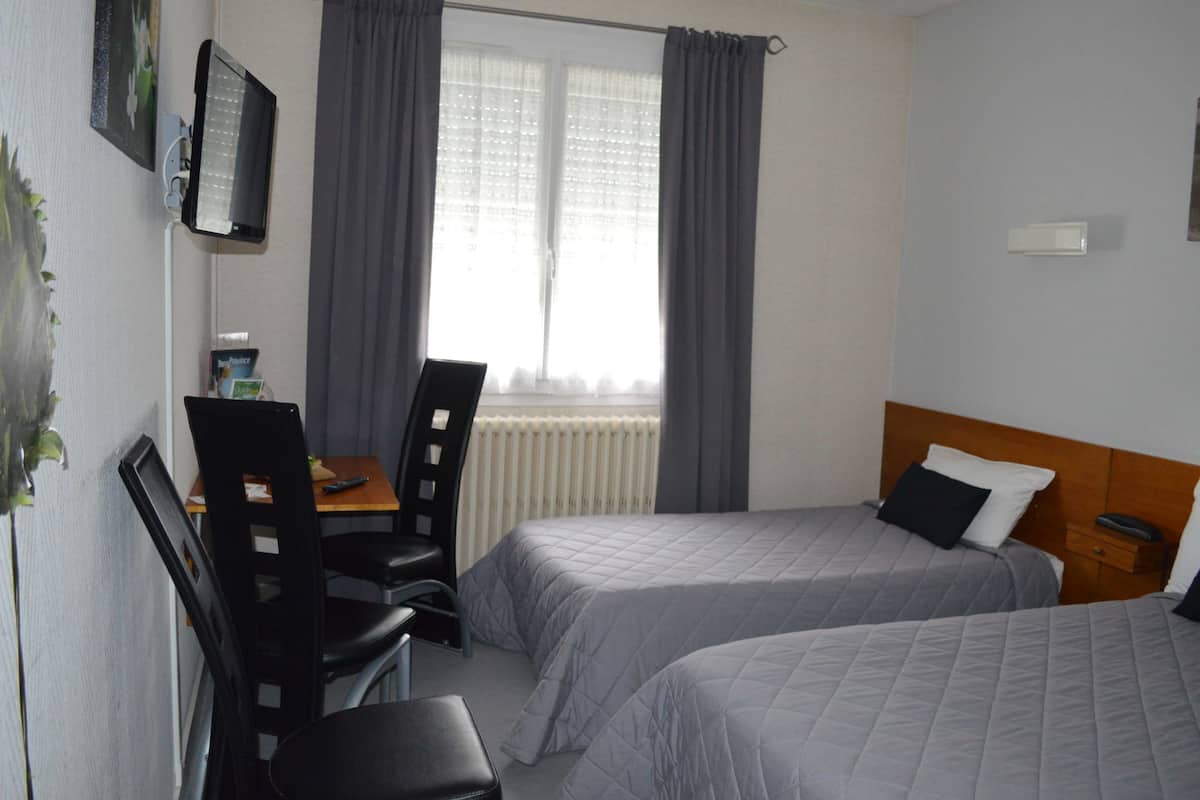 A hotel room with two beds, a desk with a chair, a radiator, and a television mounted on the wall.