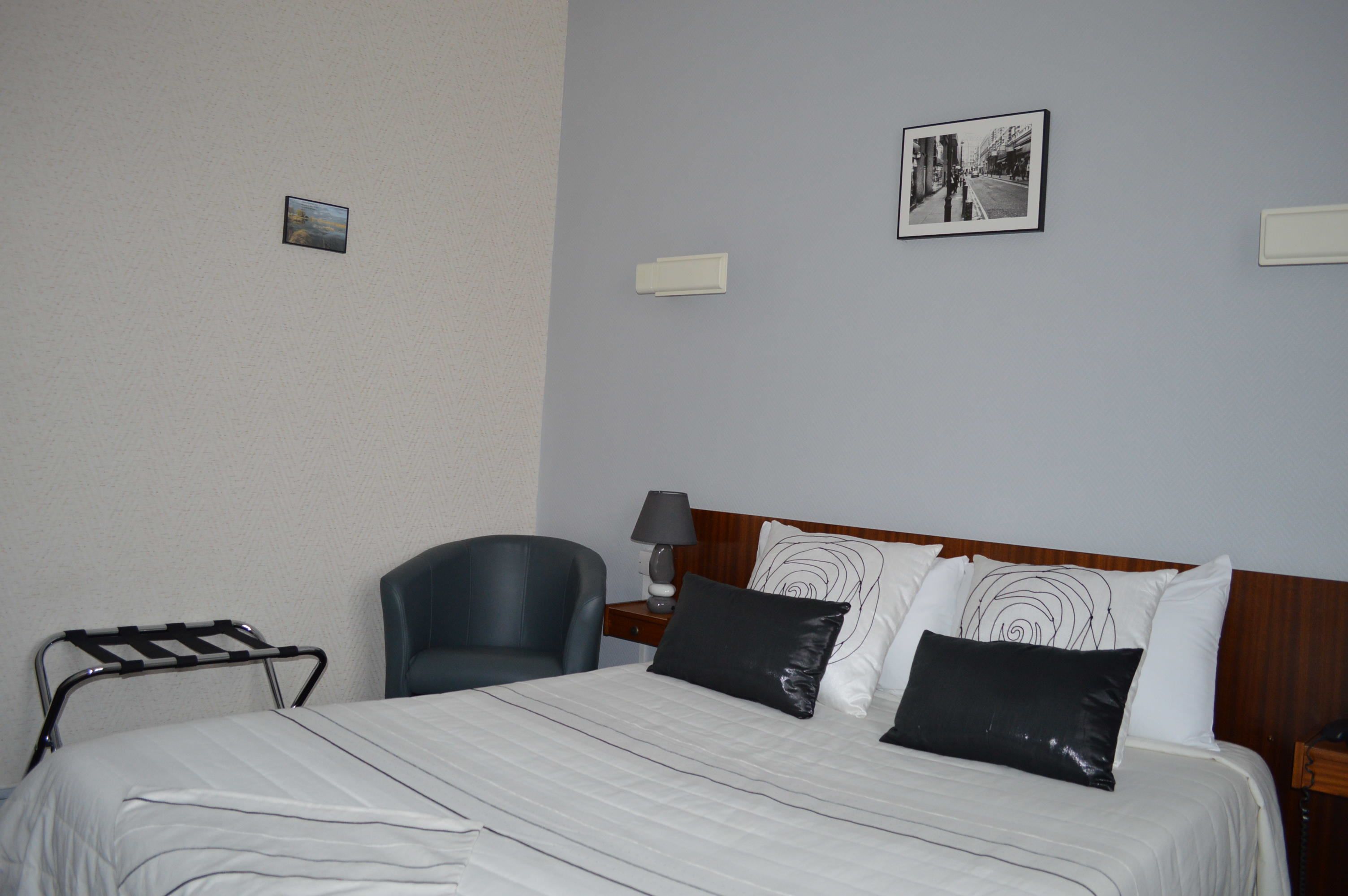 A hotel room with a bed, a chair, a nightstand, a lamp, and two wall-mounted picture frames.