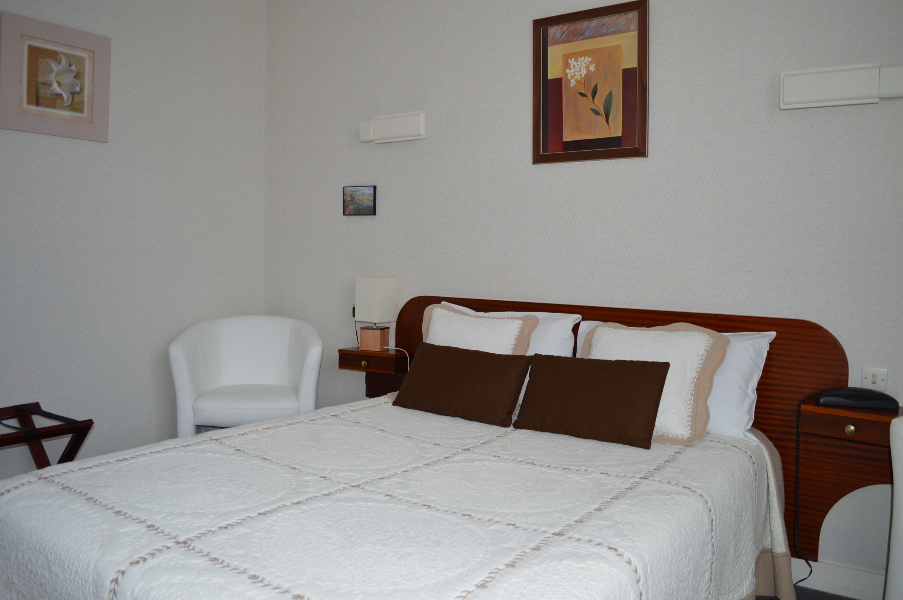 A neatly arranged hotel room with a large bed, a bedside table, a chair, and a nightstand.