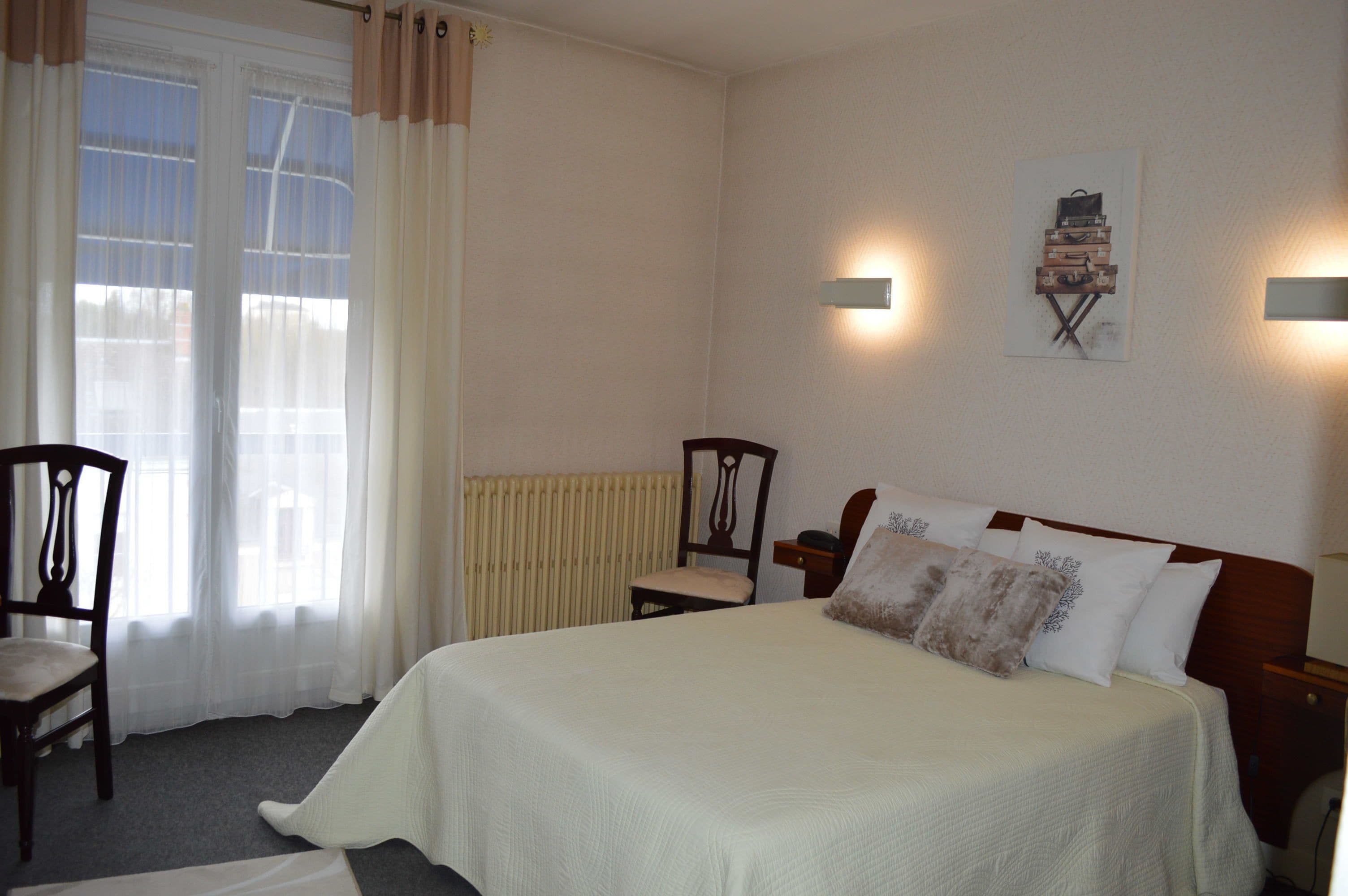 A bedroom with a bed, two chairs, a radiator, and a wall-mounted artwork.