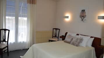 A bedroom with a bed, two chairs, a radiator, and a wall-mounted artwork.