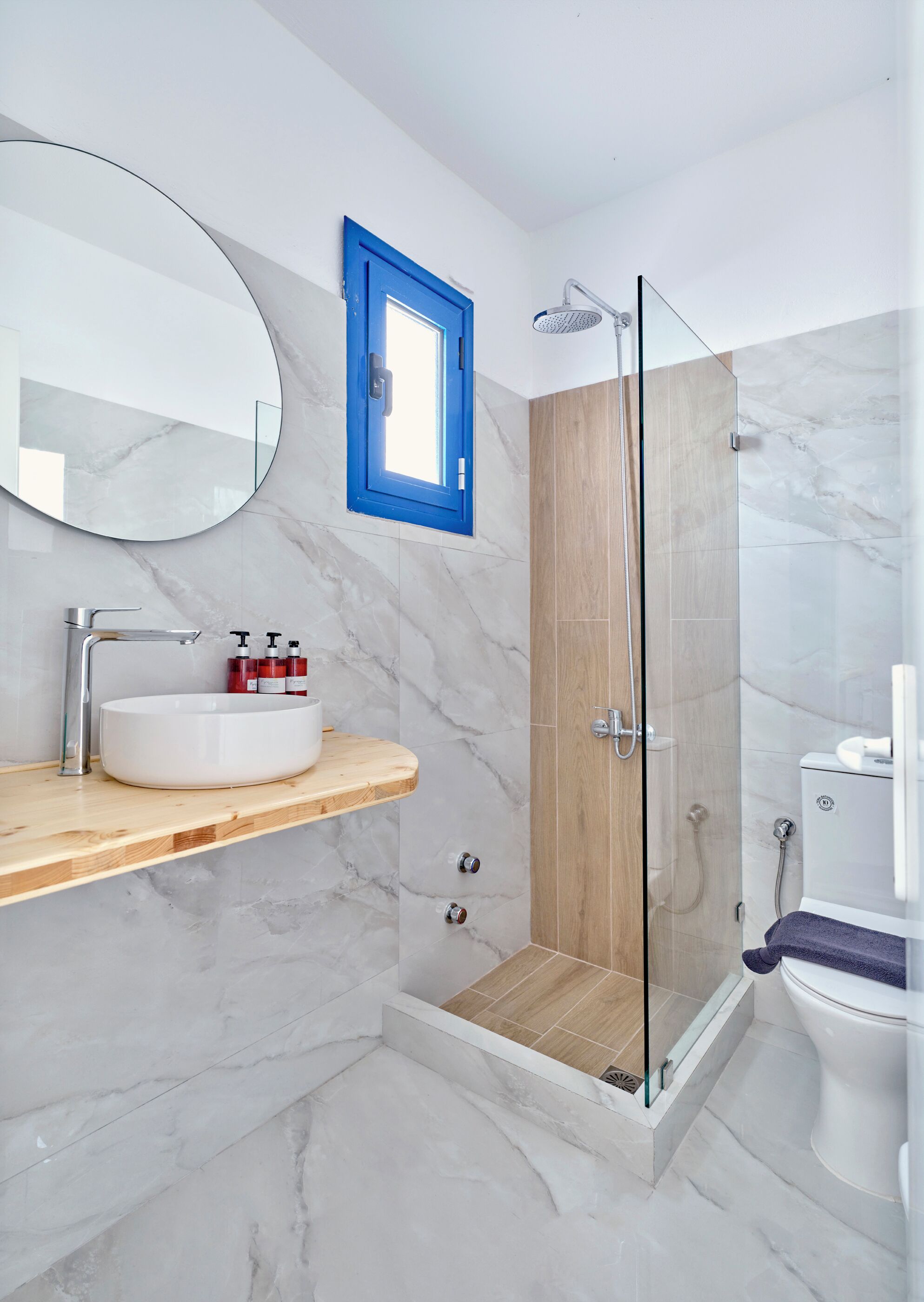 A modern bathroom with a marble sink, a glass-enclosed shower, and a wooden vanity.