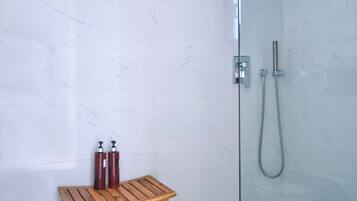 A modern bathroom with a glass shower enclosure, a wooden bench, and two red shampoo bottles.