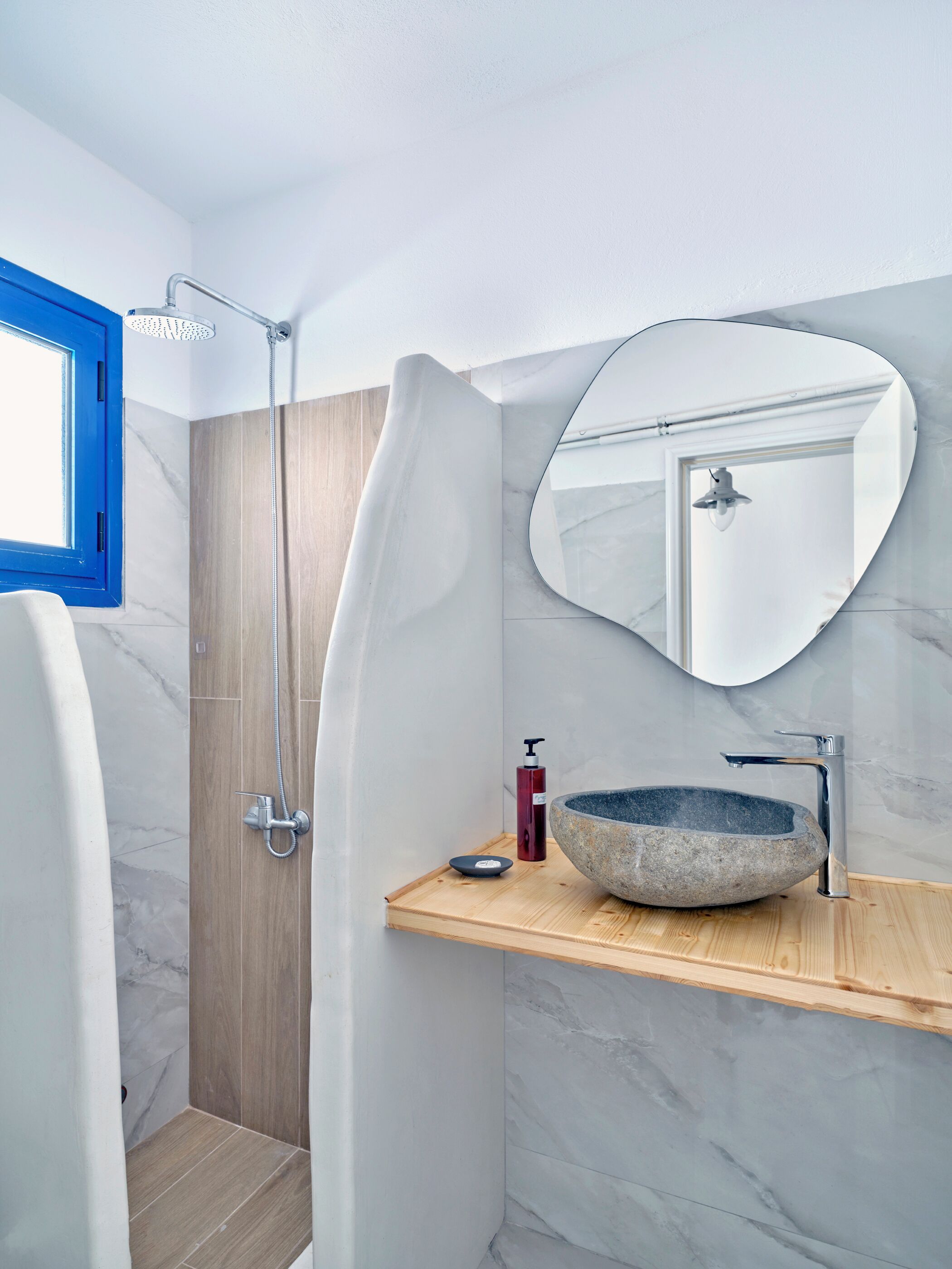 A modern bathroom with a shower, a round marble sink, and a wooden vanity.