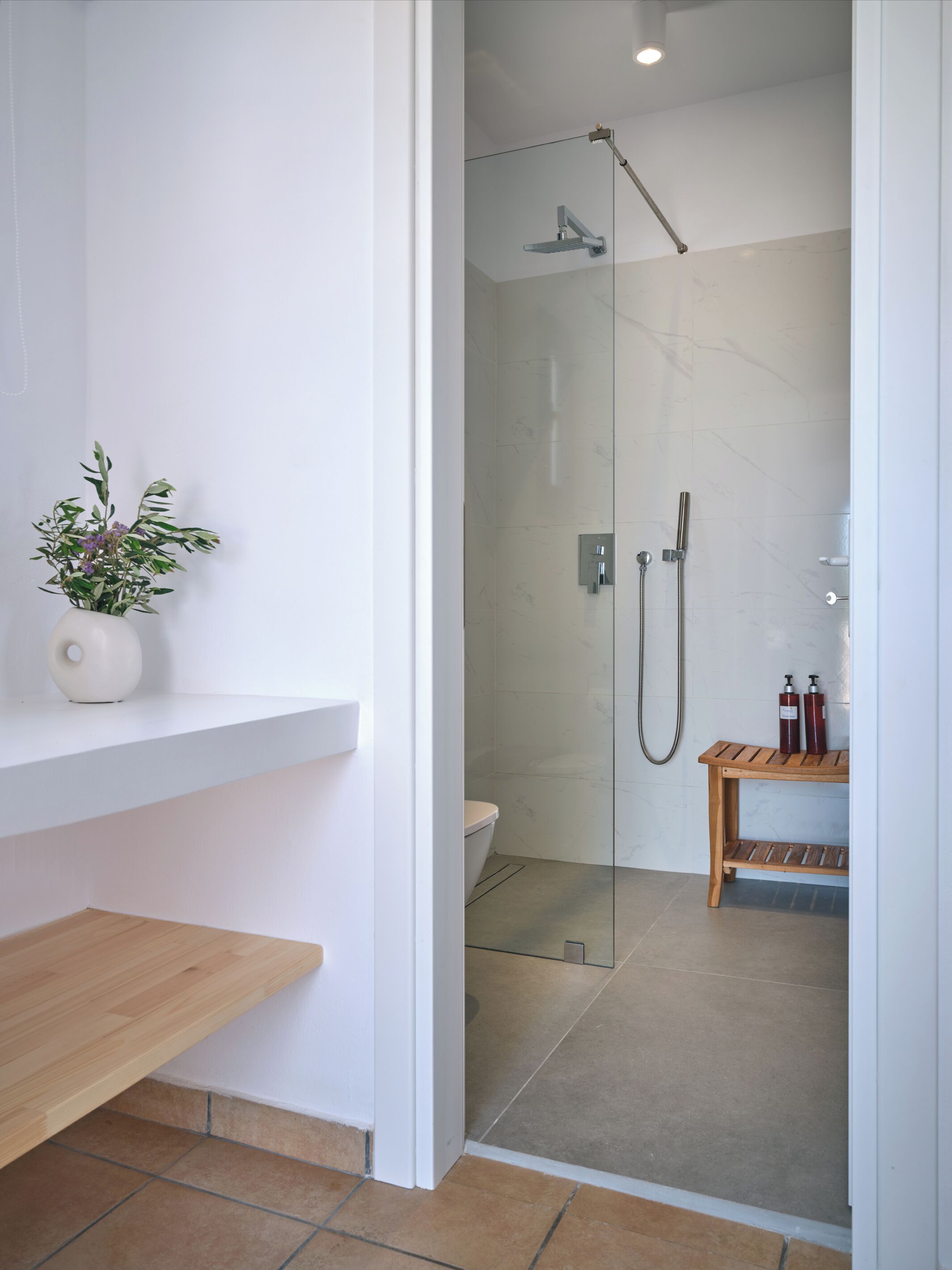 A modern bathroom with a glass shower enclosure, a toilet, and a wooden bench.