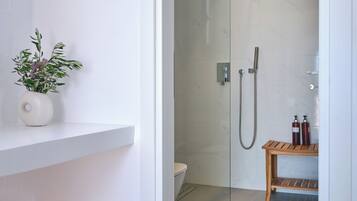 A modern bathroom with a glass shower enclosure, a toilet, and a wooden bench.