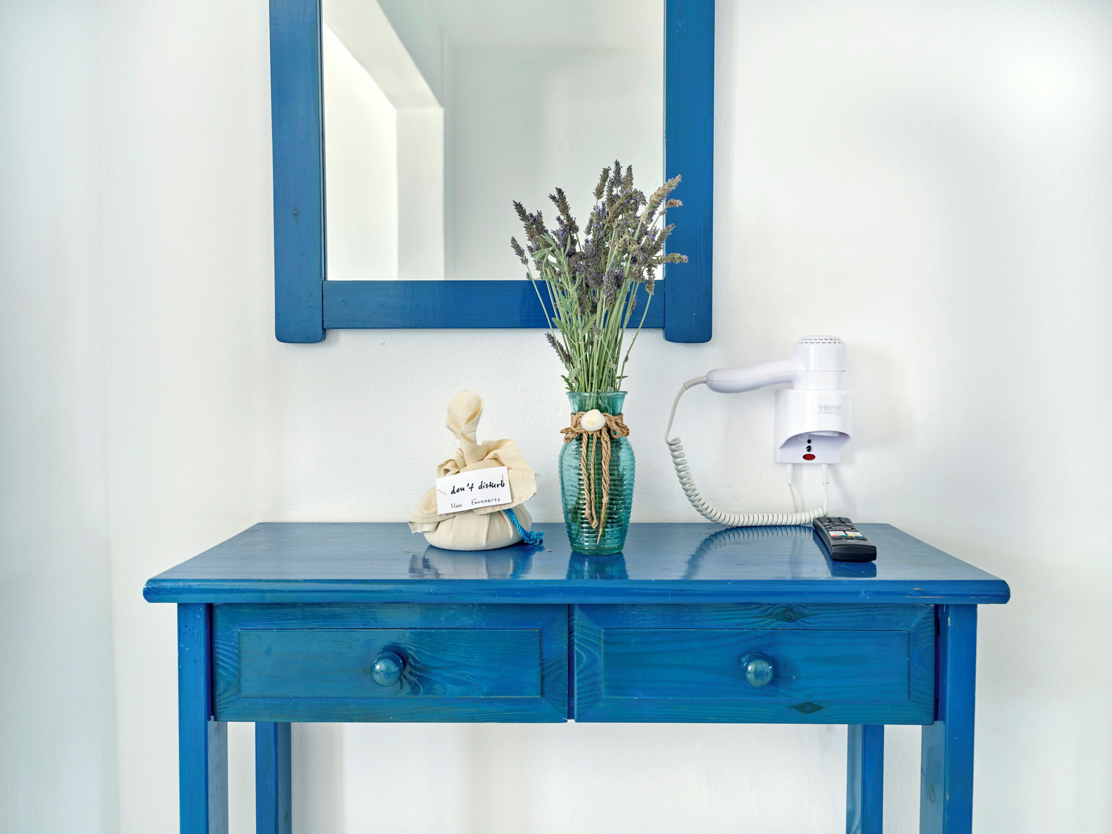 A blue dresser with two drawers, a vase with lavender, and a hairdryer plugged in.