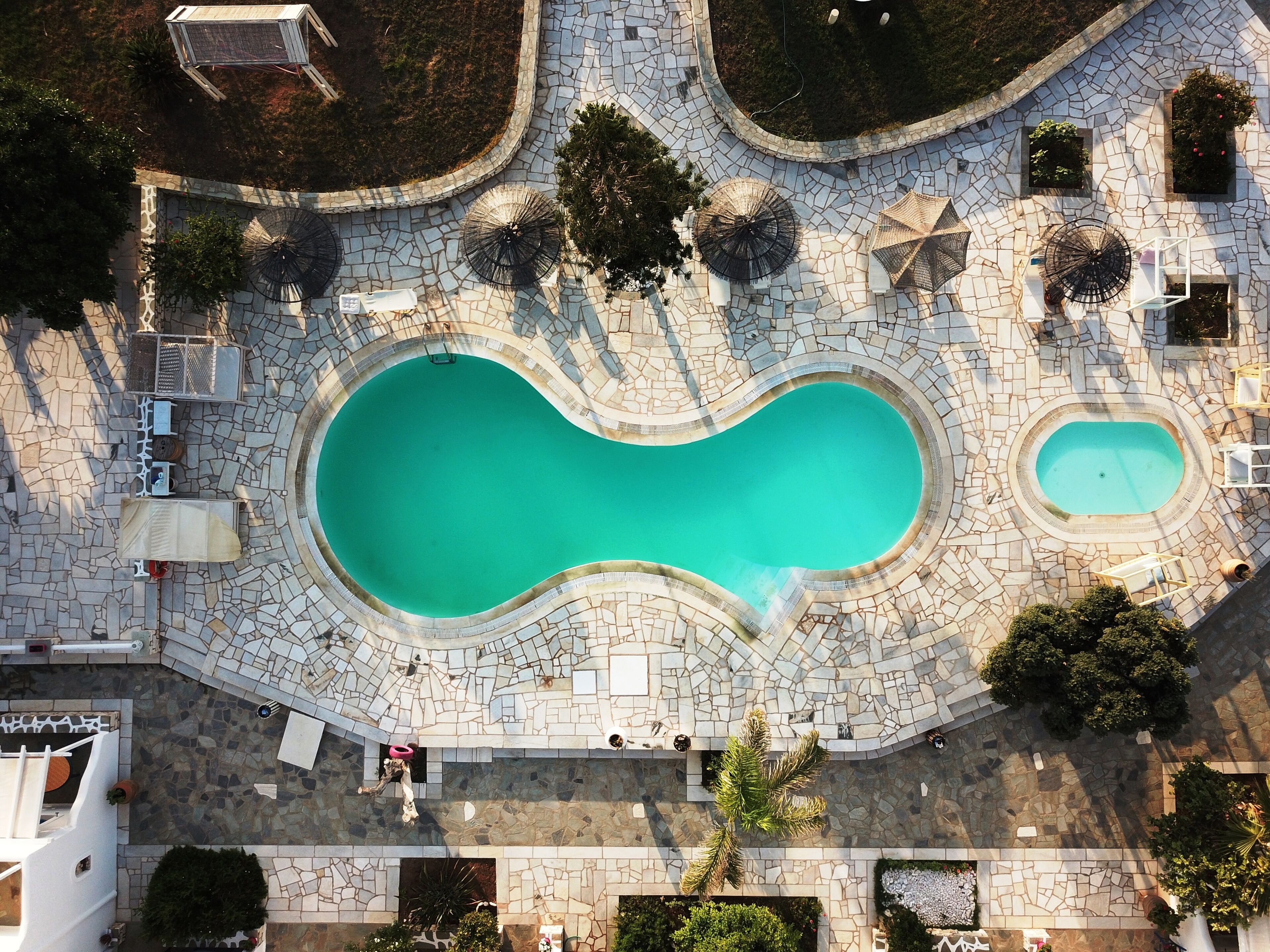 An aerial view of a swimming pool complex with two pools, surrounded by stone pathways and greenery.