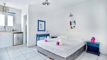 A modern hotel room with a bed, bedside tables, a desk, and a kitchenette.