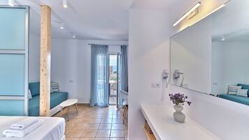 Ein modernes Hotelzimmer mit einem Bett, einer Couch, einem Schminktisch mit Spiegel und Blick ins Freie durch eine Schiebetür.