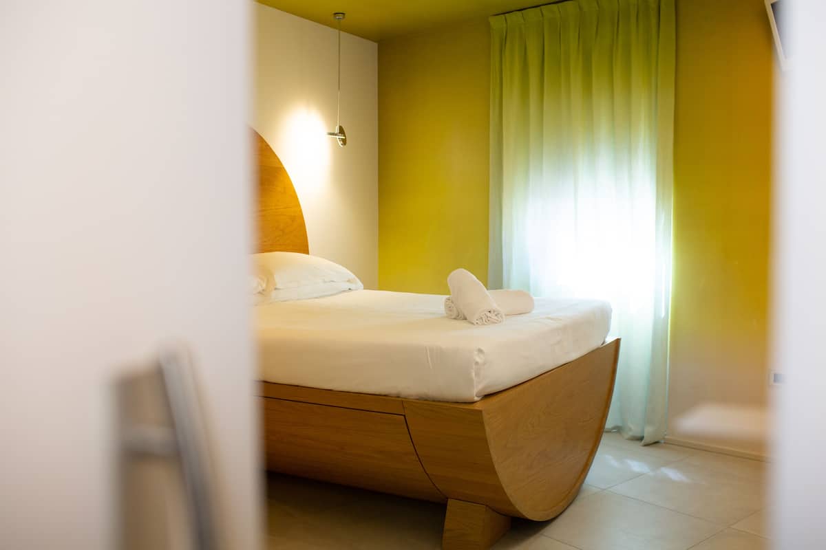 Ein modernes Schlafzimmer mit einem gewölbten Holzbett, einer weißen Matratze und einem ordentlich bezogenen Bett mit einem aufgerollten Handtuch.