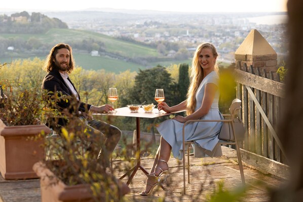 A couple seated at an outdoor table with a scenic view of a town and hills in the background.