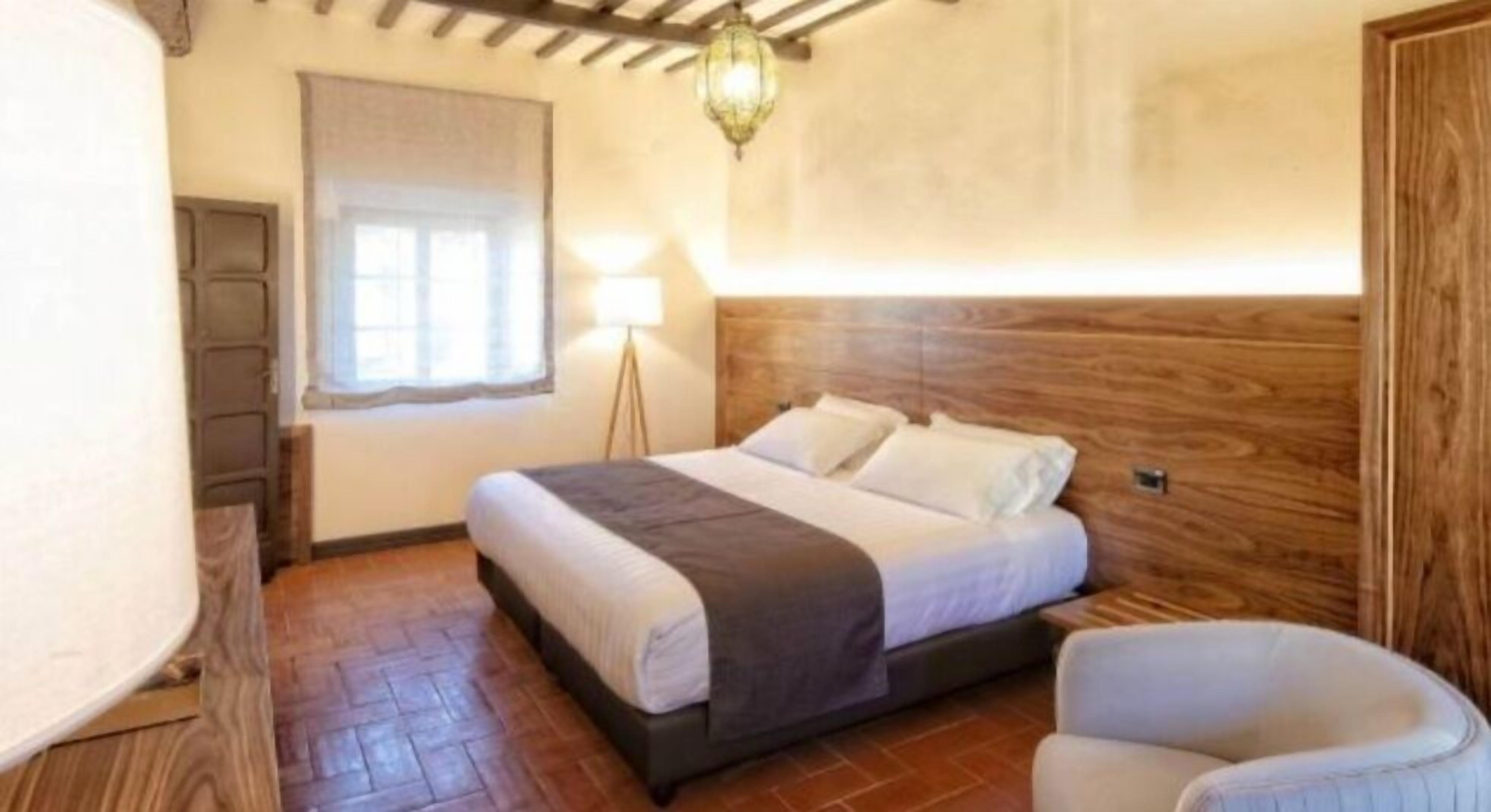 A bedroom with a wooden headboard, a bed with white linens, a floor lamp, and a chair.