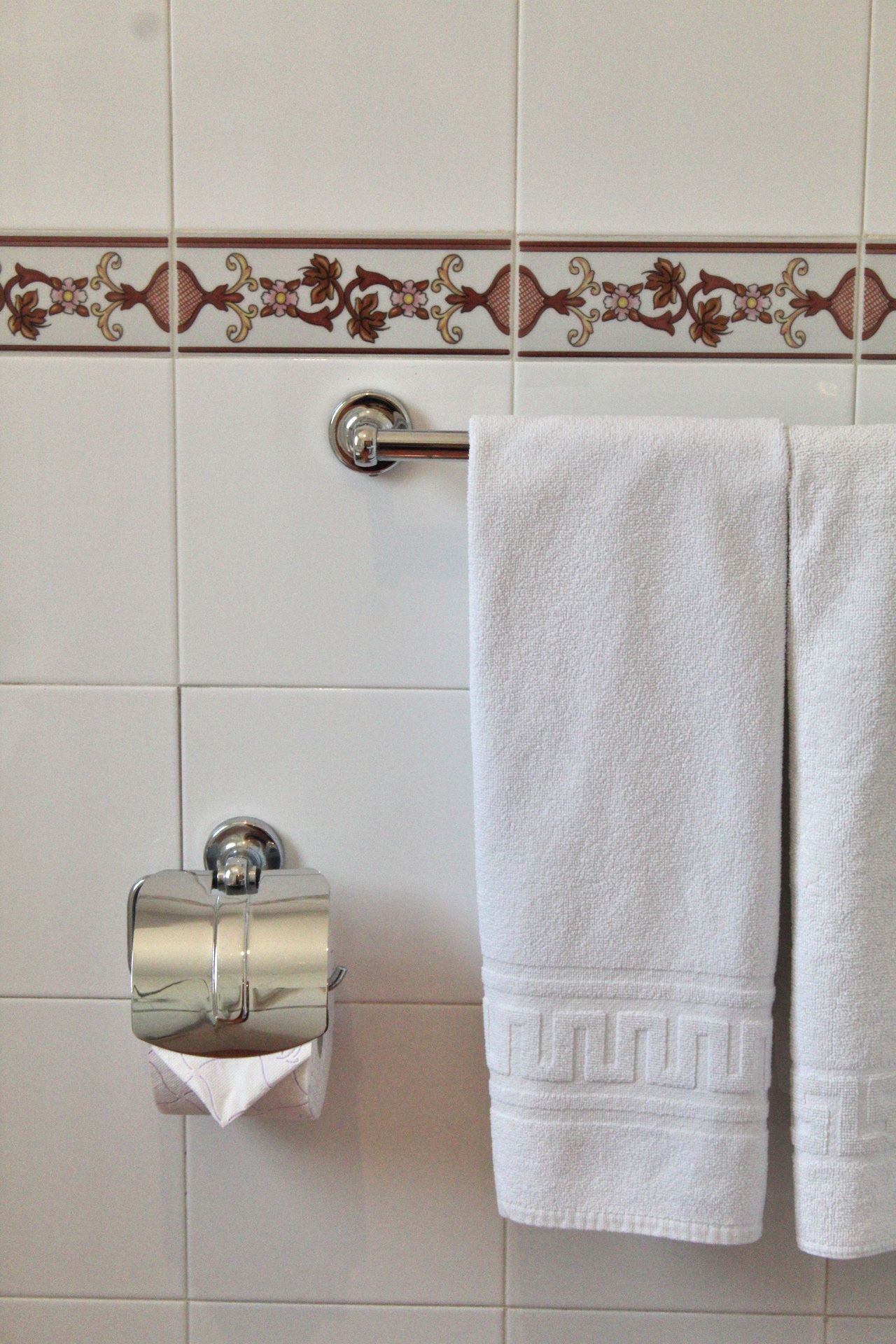 Un baño con azulejos blancos, un dispensador de papel higiénico y un toallero con una toalla doblada.