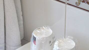 Un bagno con un lavandino bianco, due tazze avvolte nella plastica e una cornice di piastrelle decorative.