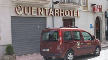 Una furgoneta roja estacionada frente a un hotel con una puerta persiana cerrada y un letrero que dice "QUENTARHOTEL".