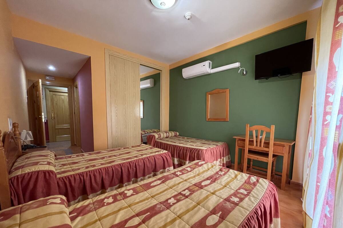 Une chambre d’hôtel avec deux lits, un bureau, une chaise, une télévision et un appareil de climatisation.