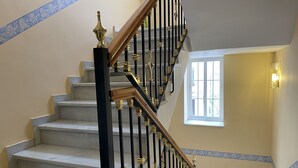 Una escala amb barana negra i daurada, trams blancs i una finestra amb vista a l'exterior.