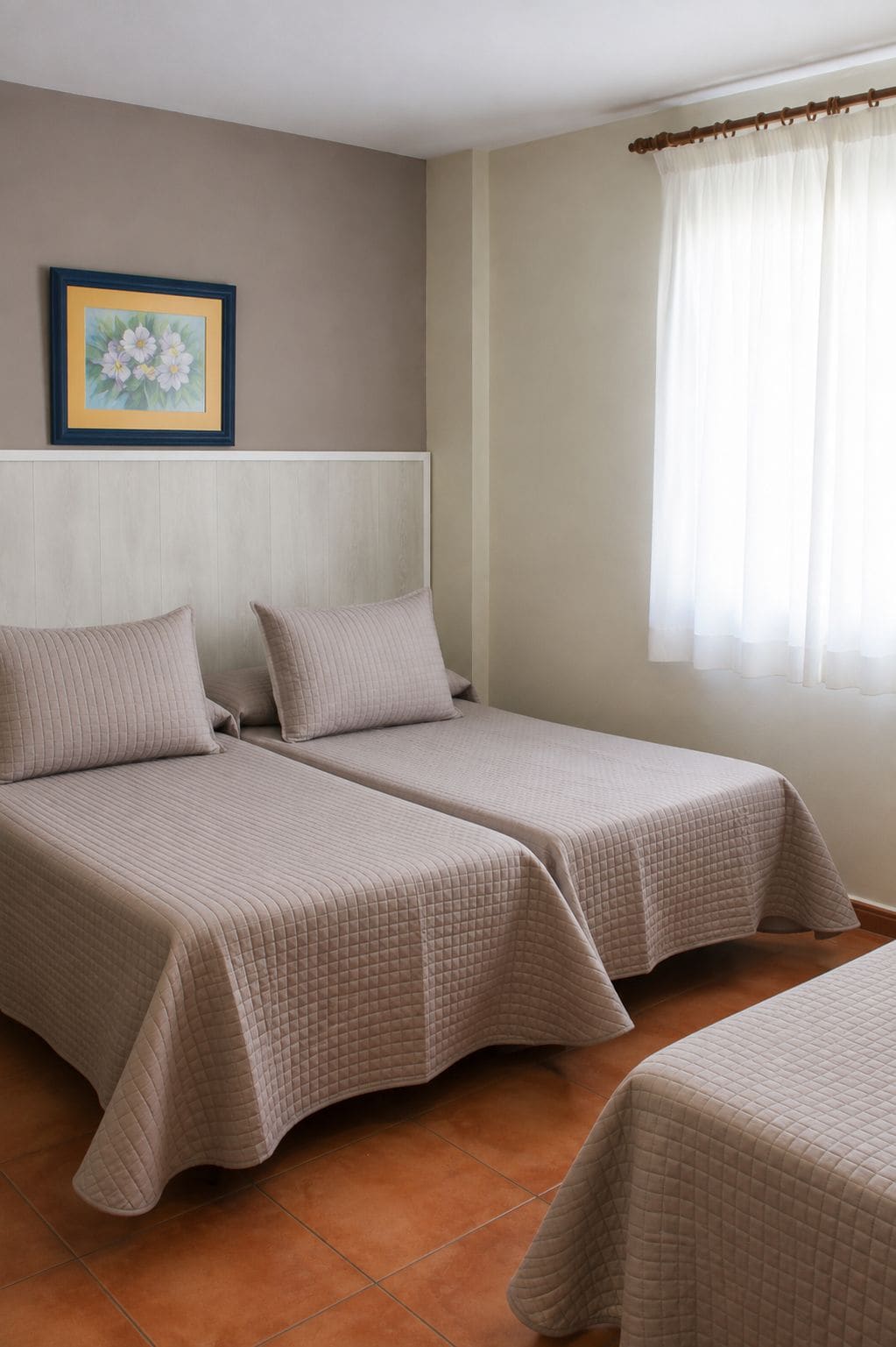 Una habitación con dos camas, cabeceras, una ventana con cortinas e imagen enmarcada en la pared.
