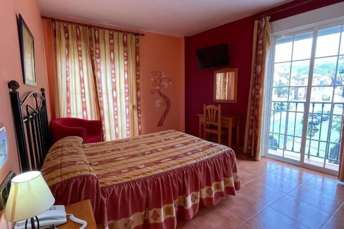 Une chambre d’hôtel avec un lit, un bureau avec une lampe, une chaise, une télévision et un balcon avec vue.