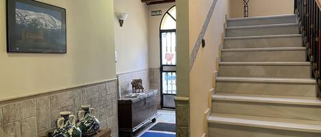 A hallway with a stone wall, a framed picture, a small table with decorative items, and a staircase with a blue mat at the bottom.