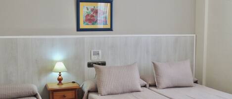 Habitación de hotel con dos camas, una mesita de noche con lámpara, un cuadro enmarcado en la pared y una bandeja sobre la cama.