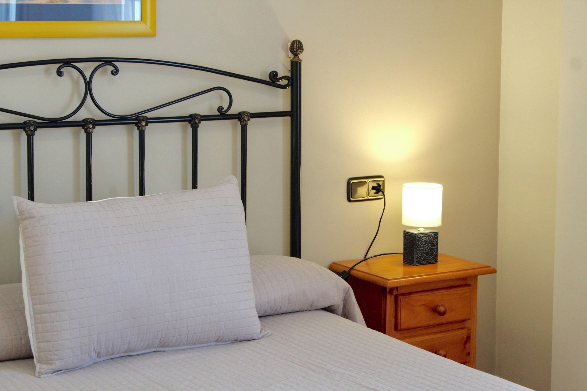 Ein Bett mit Kopfteil, ein Nachttisch mit Lampe und eine Steckdose.