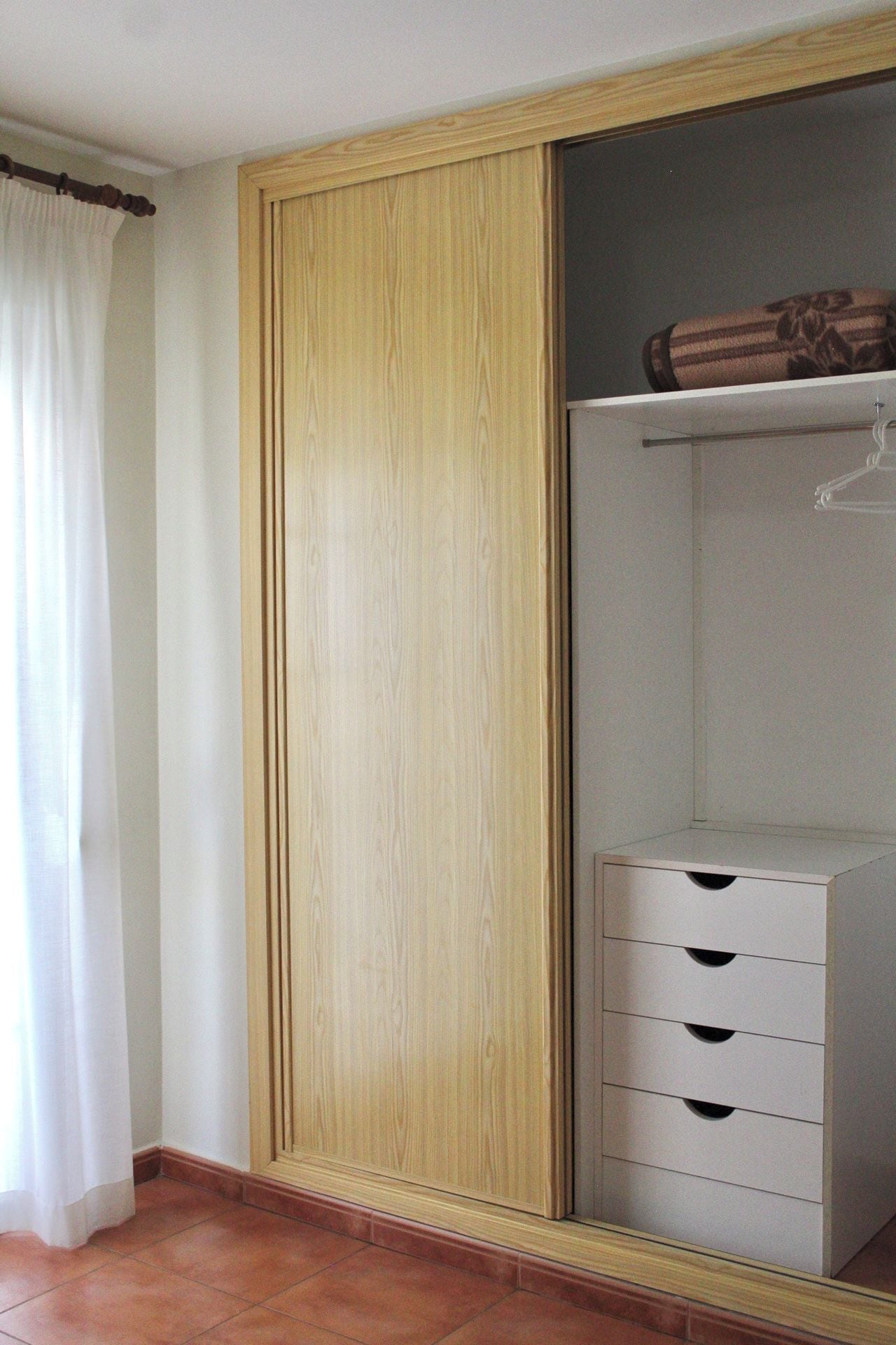 Habitación con armario de madera, cómoda blanca con cajones y espacio para colgar ropa.