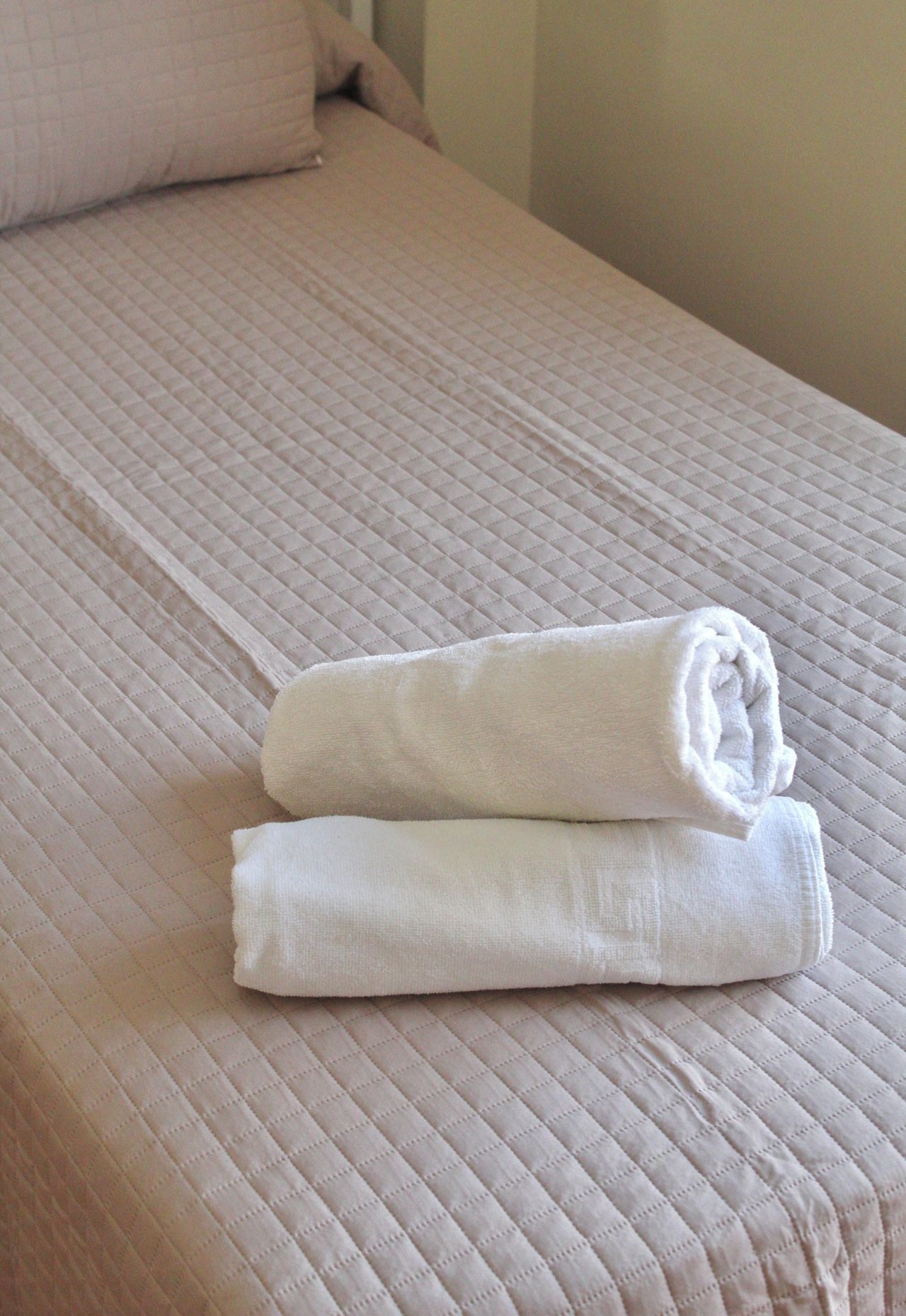 A bed with a quilted bedspread and two rolled white towels.
