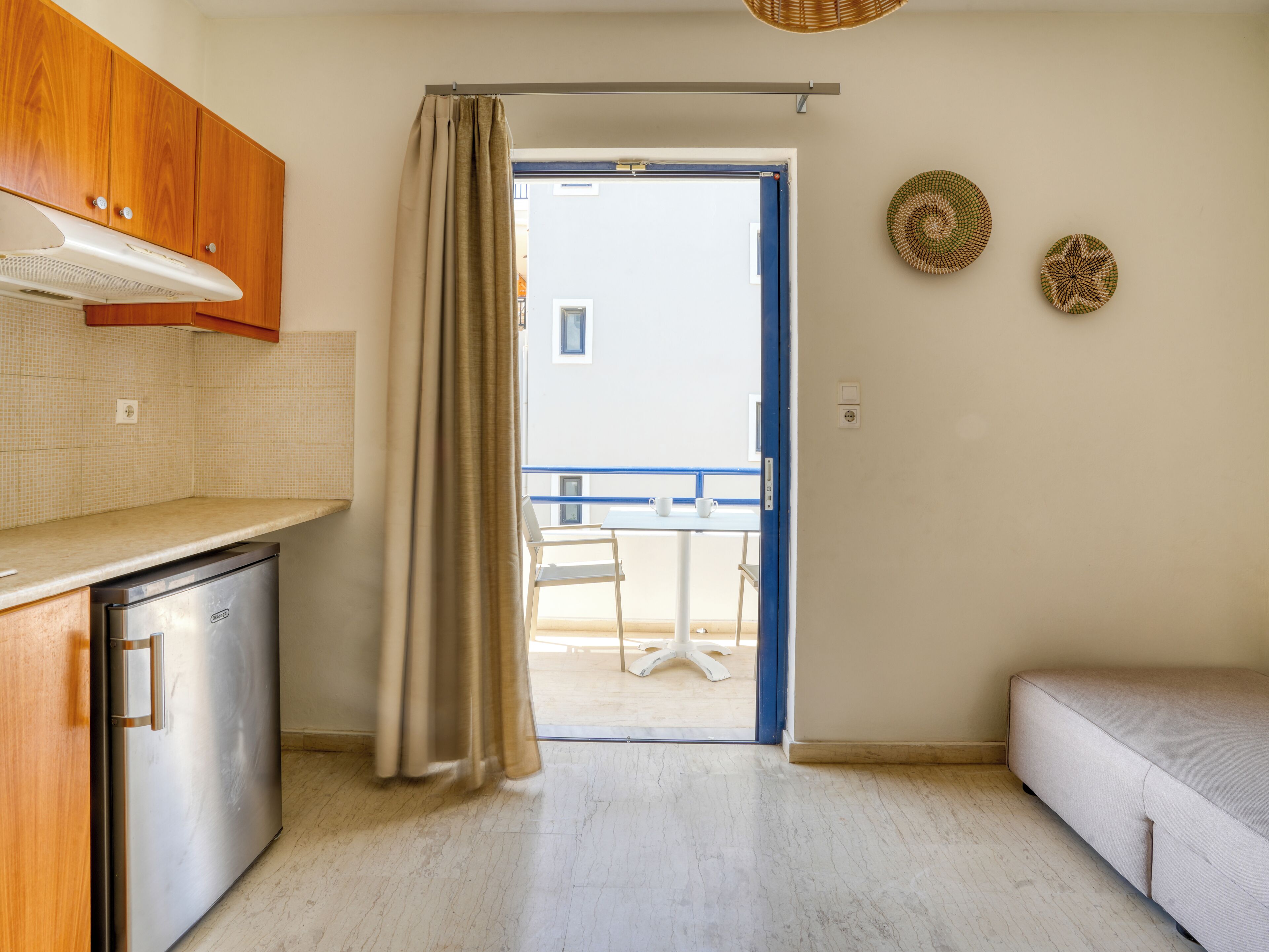 A compact kitchen with a refrigerator, a wooden cabinet, a curtain, a dining table with chairs, and a sofa.