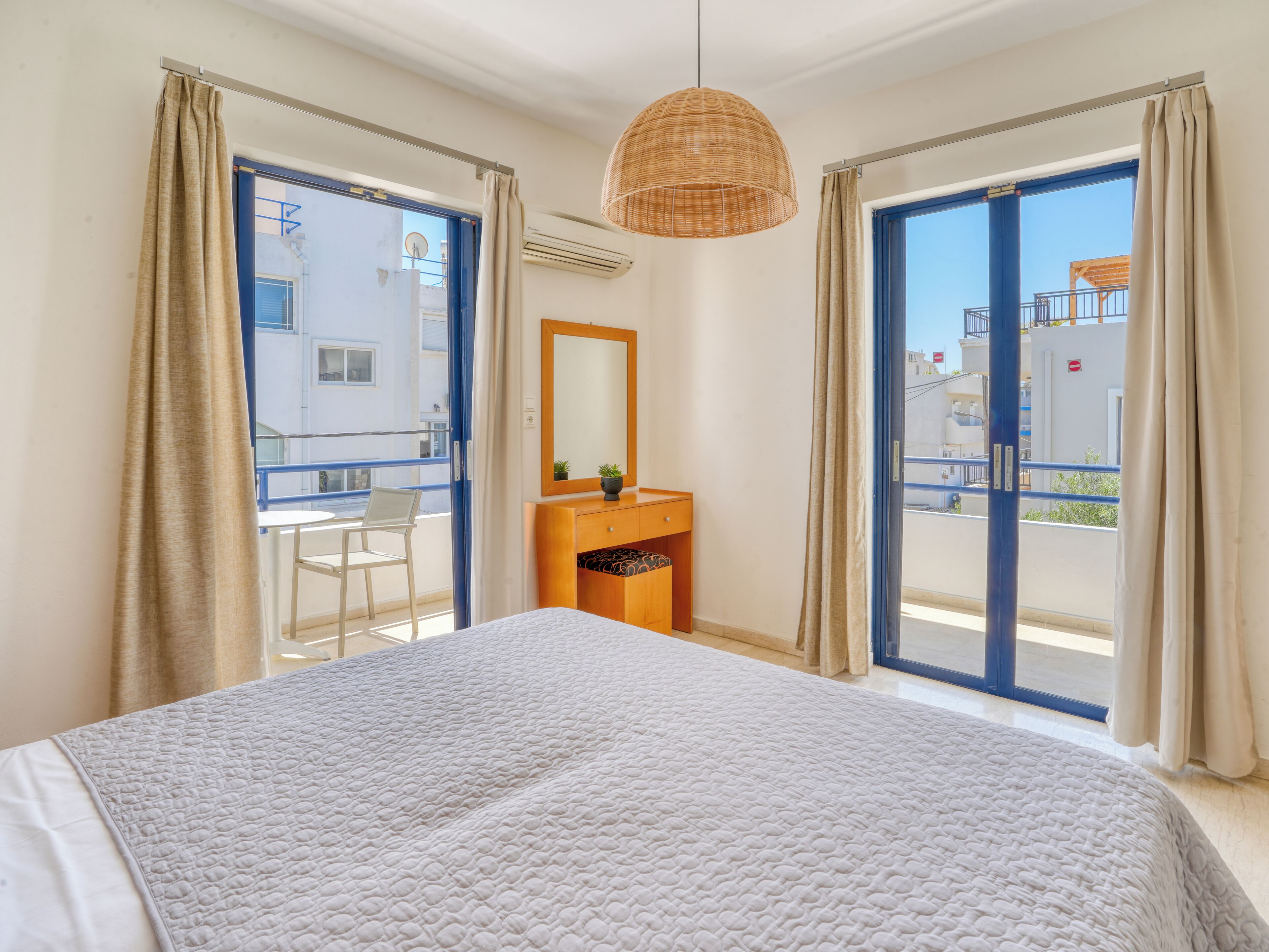 A bedroom with a bed, a dresser, a mirror, and a balcony with a view of buildings.