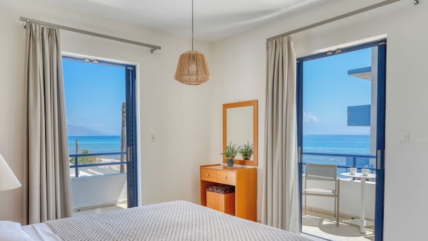 Quarto de hotel com cama, penteadeira, espelho e varanda com vista para o mar.
