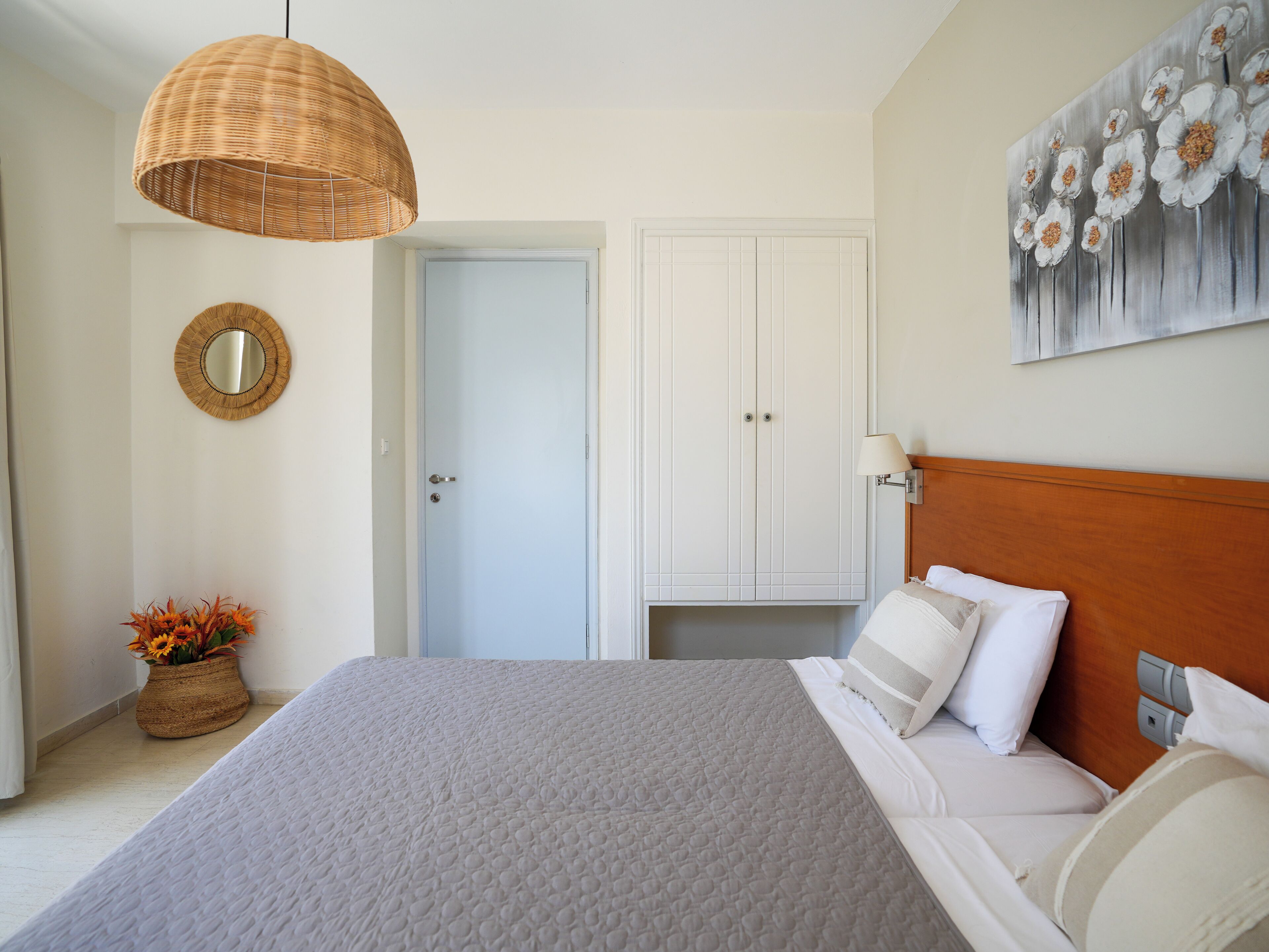 Un dormitorio con una cama, una lámpara colgante, una puerta, un espejo y un cuadro.