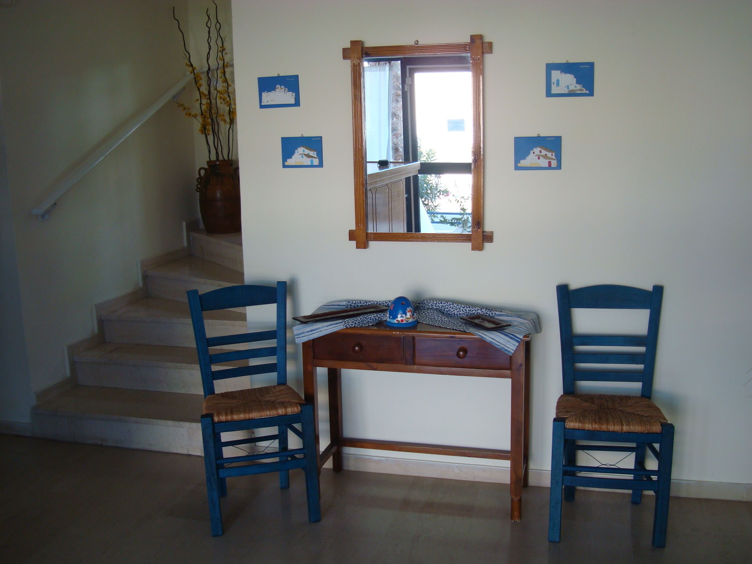 Una habitación con un escritorio de madera, dos sillas azules, un espejo y una escalera.
