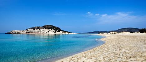 Una spiaggia con acque cristalline turchesi, una riva sabbiosa e affioramenti rocciosi.