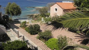 A coastal property with a paved patio, a small building with a tiled roof, and a view of the sea and mountains in the distance.