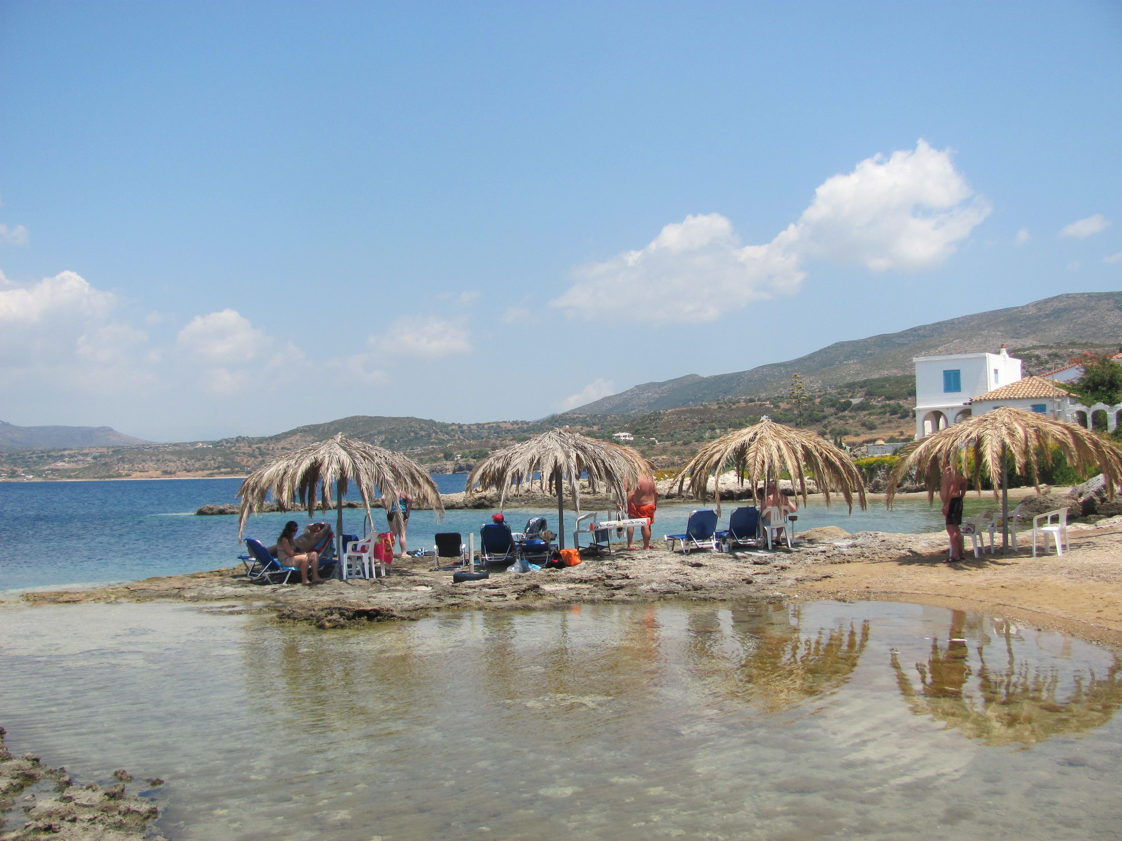 A beach with clear waters, umbrellas, and a white building in the background.