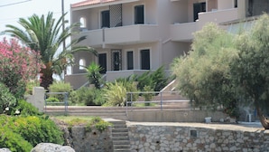 A coastal building with a stone staircase leading to a balcony, surrounded by greenery and a rocky shoreline.