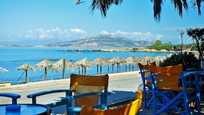 A seaside terrace with chairs and tables, a view of the sea, and a mountain in the background.
