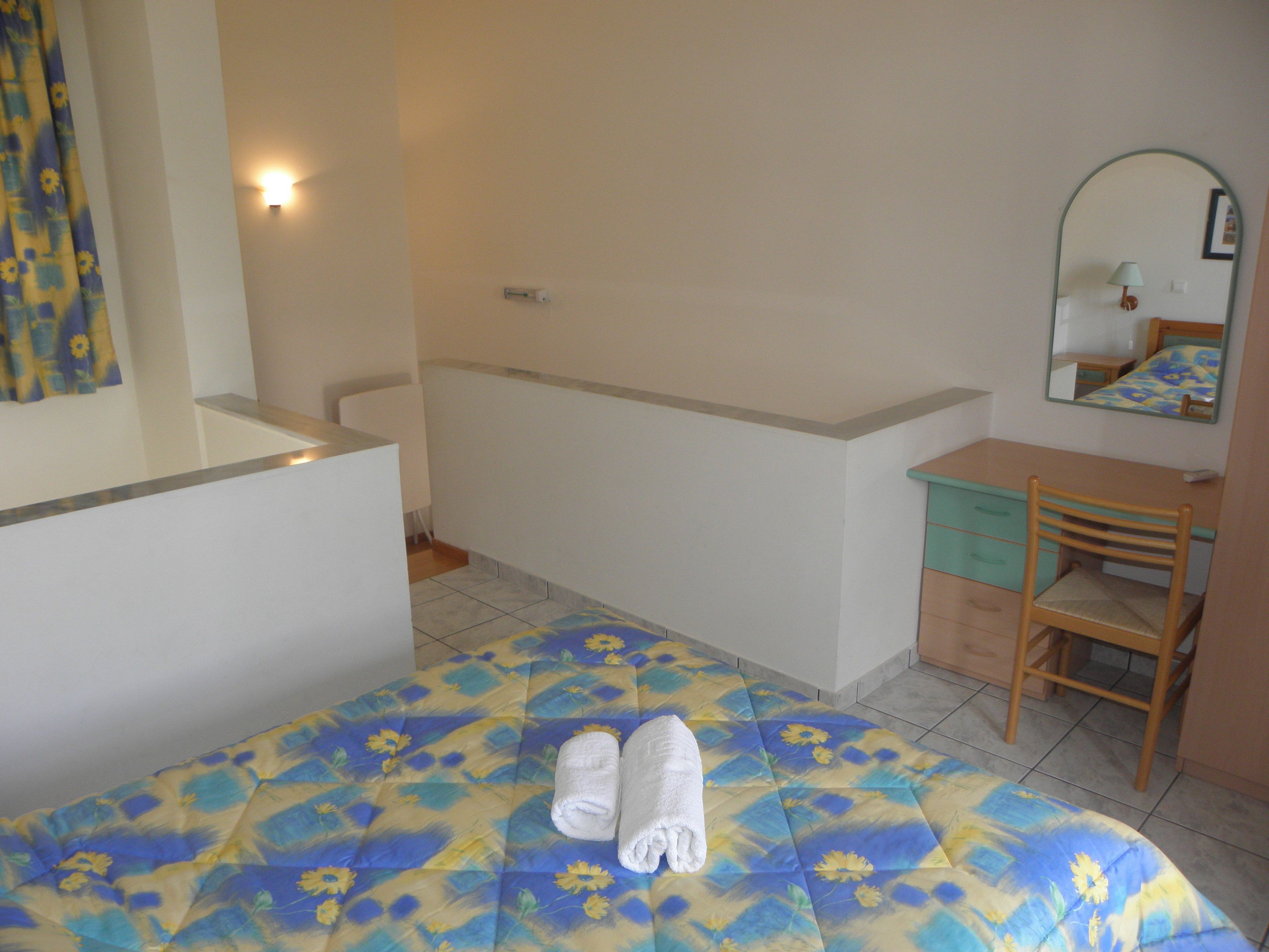 A bedroom with a bed, a chair, a desk, a mirror, and a bathroom with a bathtub.