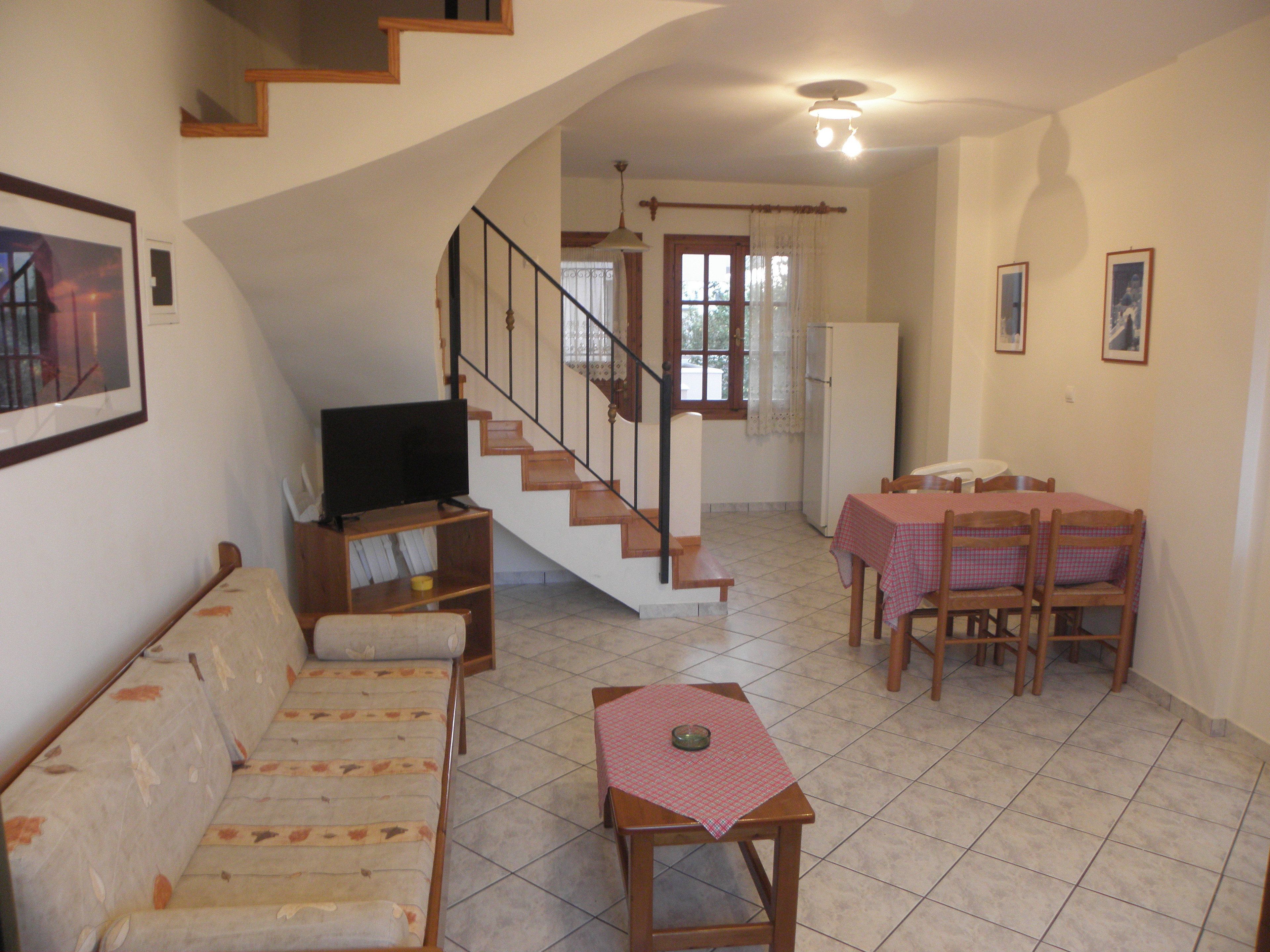 Un salon comprenant un canapé, un téléviseur, une table à manger avec des chaises et un escalier.