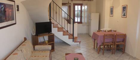 Un salon comprenant un canapé, un téléviseur, une table à manger avec des chaises et un escalier.