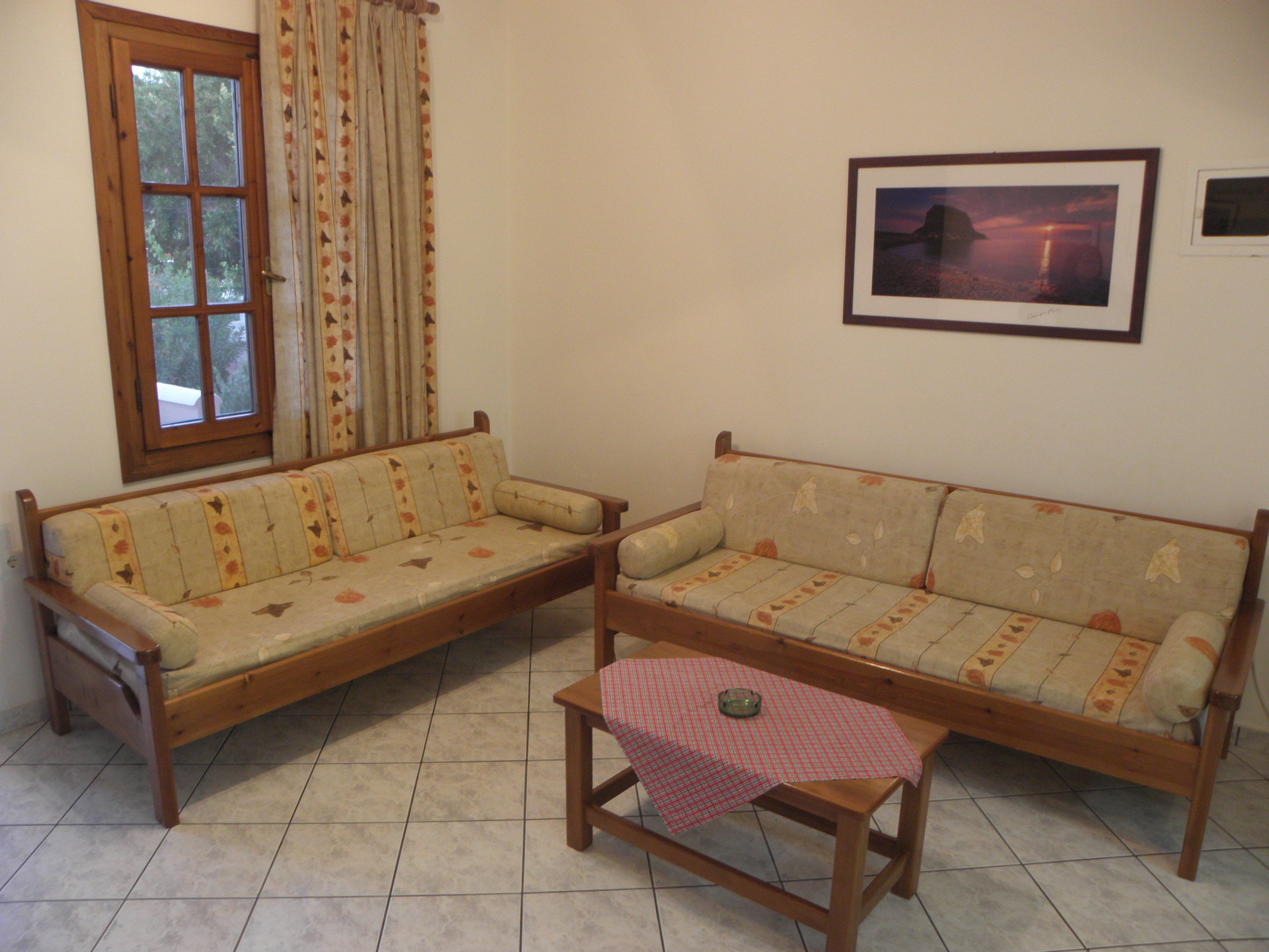 Una sala de estar con dos sofás, una mesita, una ventana con cortinas y un cuadro en la pared.