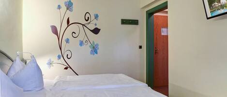 A hotel room with a bed, pillows, a wall decoration, a door, and a framed picture on the wall.