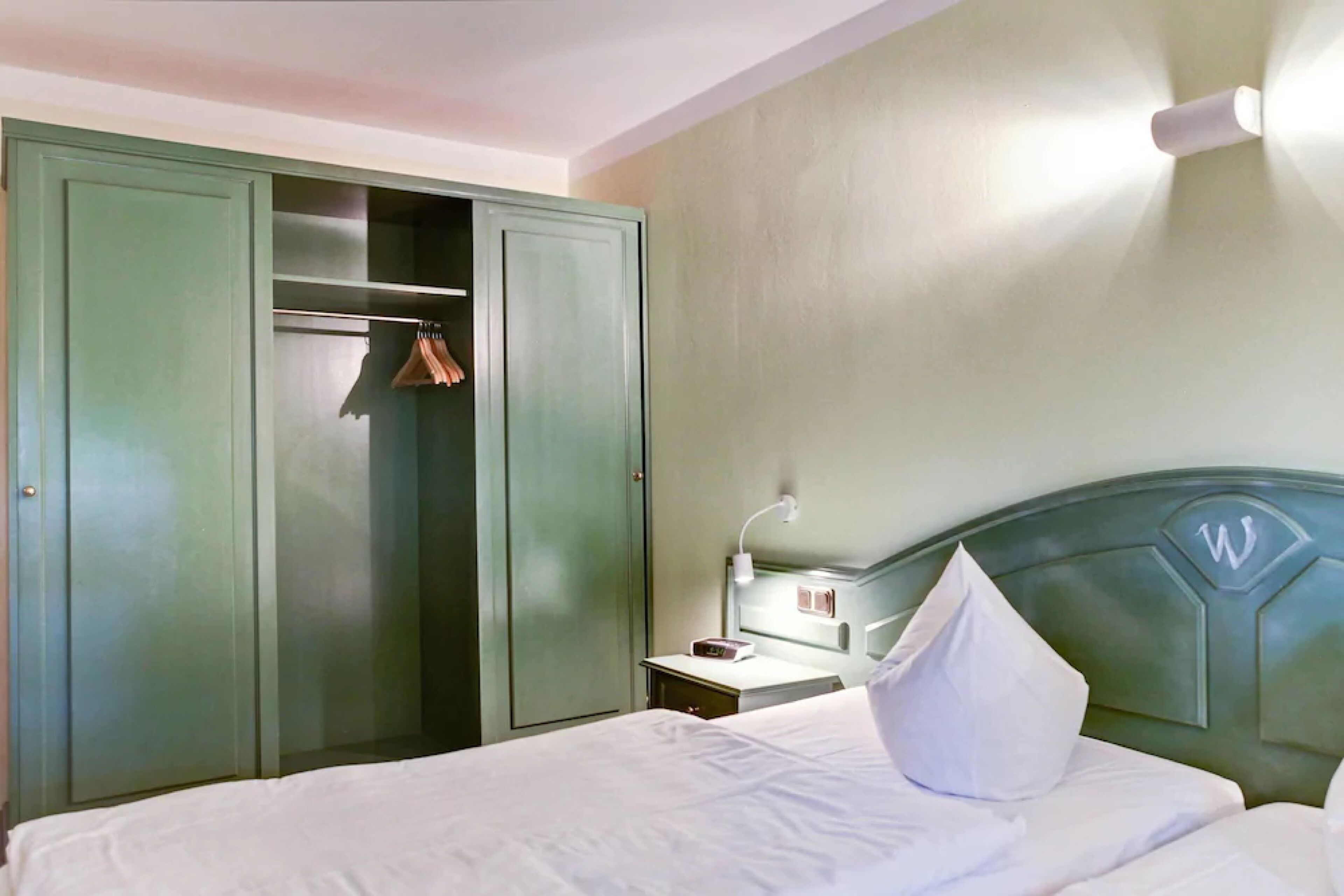 A hotel room with a bed, a nightstand, a lamp, a wardrobe, and a closet.