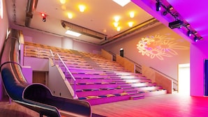 A modern auditorium with tiered seating, a stage, and a large screen displaying floral projections. - Familienresort Usedom (Trassenheide)