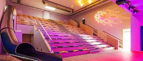 A modern auditorium with tiered seating, a stage, and a large screen displaying floral projections.