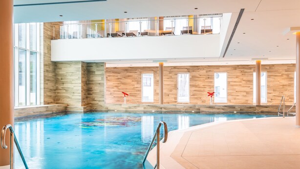 An indoor swimming pool with a second level balcony, large windows, and a wooden wall design. - Familienresort Usedom (Trassenheide)